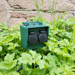 dunkelgrüne Gartensteckdose mit 4 Steckplätzen  in der Wiese montriert mit Erdspieß